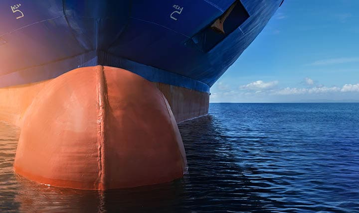Close up of large blue merchant crago ship in the middle of the ocean underway. Performing cargo export and import operations with sun rays, horizon line and beautiful sky.